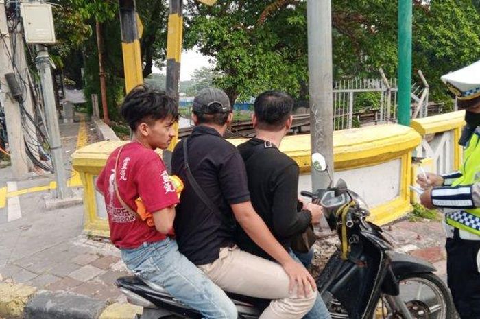 Polisi menilang pengendara Honda Supra X 125 yang dipakai bonceng tiga kuli bangunan di perempatan Karet Bivak, Tanah Abang, Jakarta Pusat