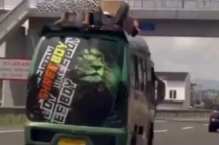 Dua pria tampak tiduran santai di atas atap Isuzu Elf yang melaju di tol Purbaleunyi