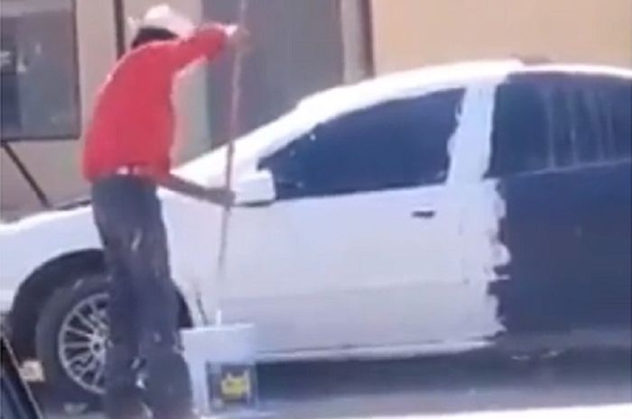 Seorang pria mengecat mobil menggunakan cat tembok