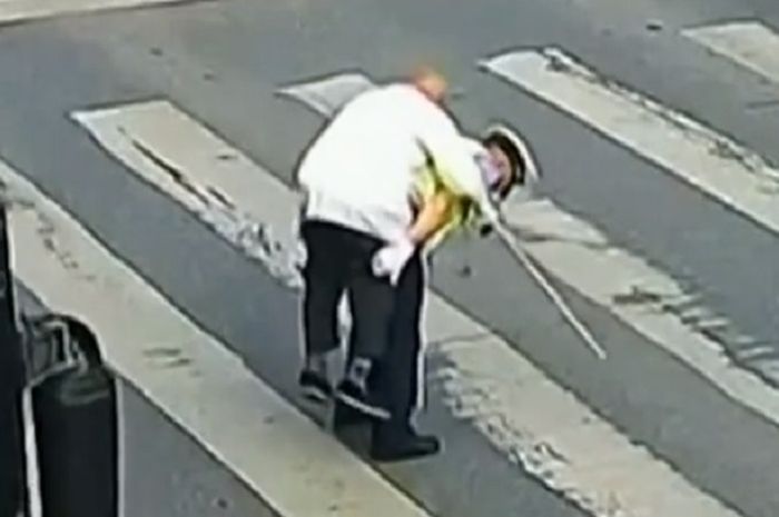 Polisi menggendong seorang kakek untuk menyebrang jalan.