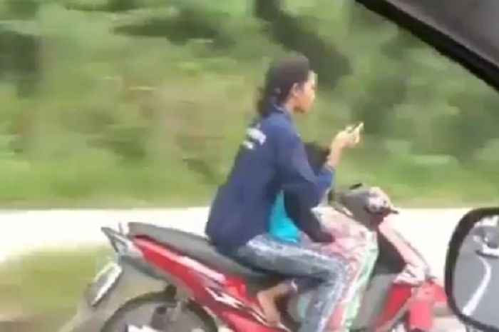 Perempuan nekat lepas setang sambil main ponsel, padahal sangat berbahaya.