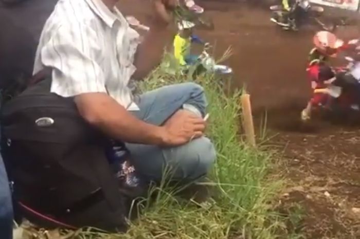 Seorang laki-laki sedang menonton balap motor sambil mengunyah rumput