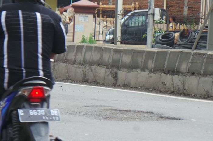 Seorang pengendara sepeda motor tengah melintas di dekat lubang di jalan arteri pantura kota tegal