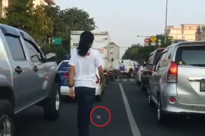 Seorang pria memungut sampah yang dibuang dari mobil Polisi