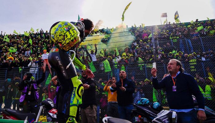 Valentino Rossi melemparkan sarung tangan dan helm khusus yang dibuat untuk tampil di Emilia Romagna ke arah tribun penonton