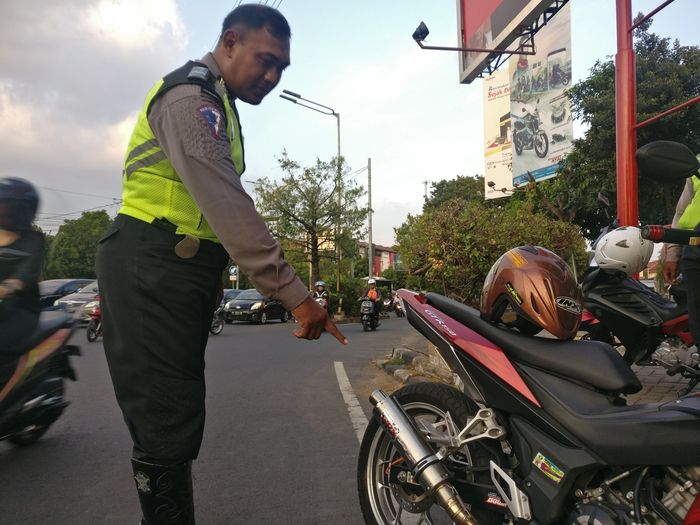 Ilustrasi polisi menunjukan pelanggaran berupa pemakaian knalpot tidak sesuai standar