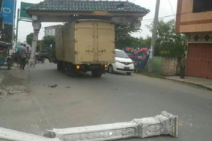 Truk warna kuning saking tingginya boks belakang sampai mencabut gapura kampung dan dibopongnya berjalan