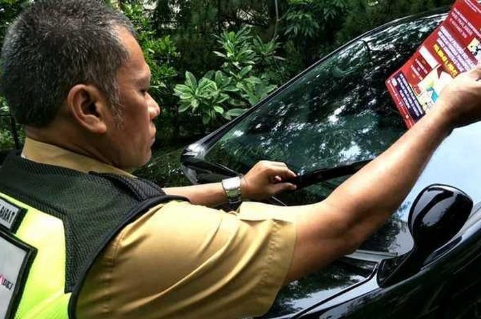 Petugas Samsat Jakarta Barat saat memberikan brosur atau selembaran peringatan di kaca mobil yang menunggak pajak, Senin (10/12). 