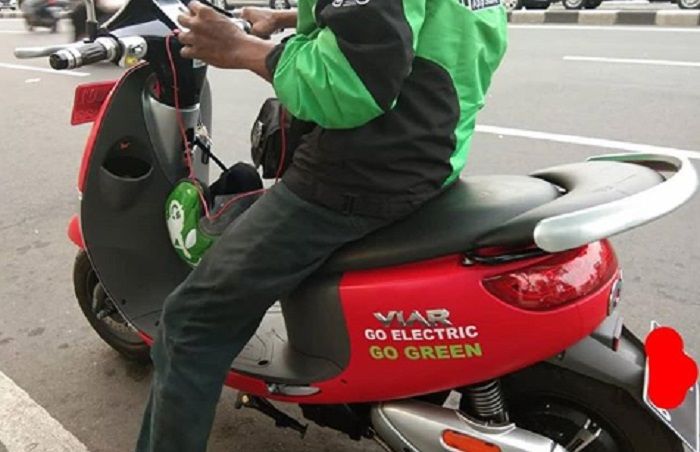 Seorang driver ojek online menggunakan motor listrik.