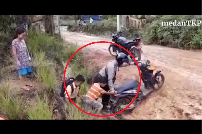 Seorang polisi membantu dua orang bocah yang terperosok ke parit