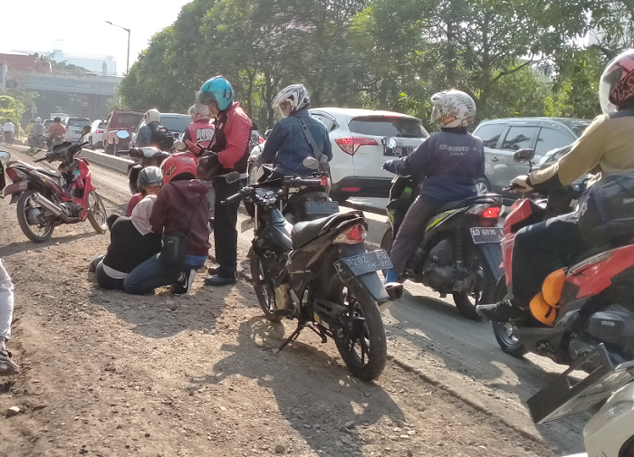 Pengendara sepeda motor terjatuh melintas di perbaikan jalan.