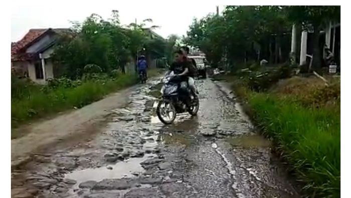 Warga melintasi jalan rusak penuh genangan di Desa Cikeusal, Kecamatan Ketanggungan, Brebes, Jawa Tengah