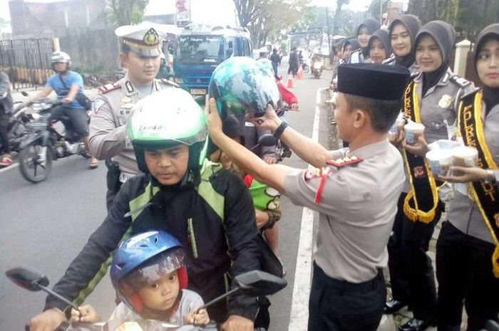 Kapolres Garut memasangkan helm kepada istri seorang pemotor yang melintas di depan Mapolres Garut, Kamis (17/5/2018).(KOMPAS.com/ARI MAULANA KARANG)