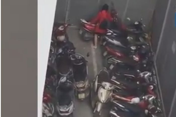 Seorang wanita berusaha mengeluarkan motornya yang terjebak di parkiran sempit