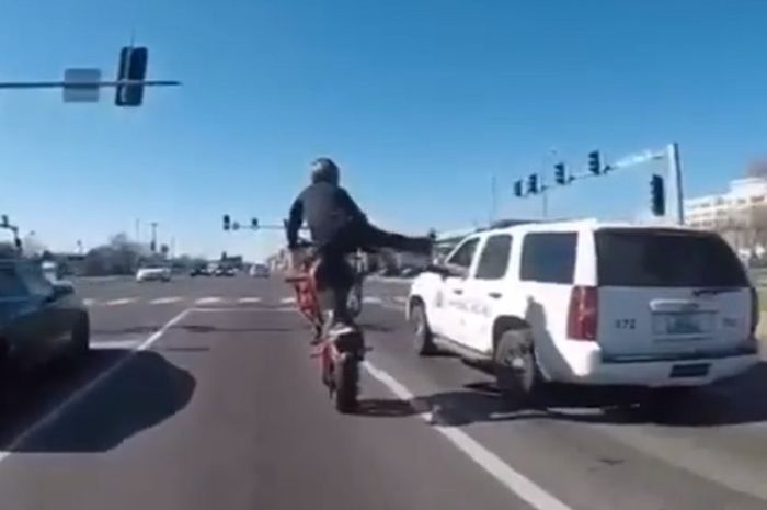 Biker wheelie di samping mobil polisi