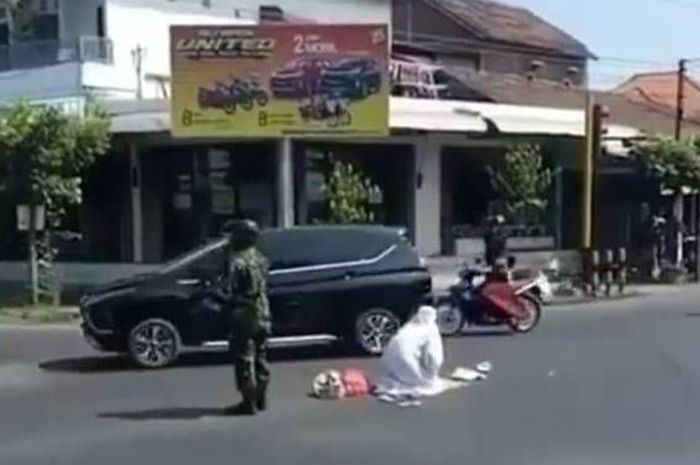 seorang wanita lakukan gerakan sholat di tengah perempatan jalan dengan dijaga seorang TNI di daerah Tulungagung