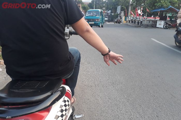 Ilustrasi pengendara motor memberi isyarat tangan di persimpangan jalan