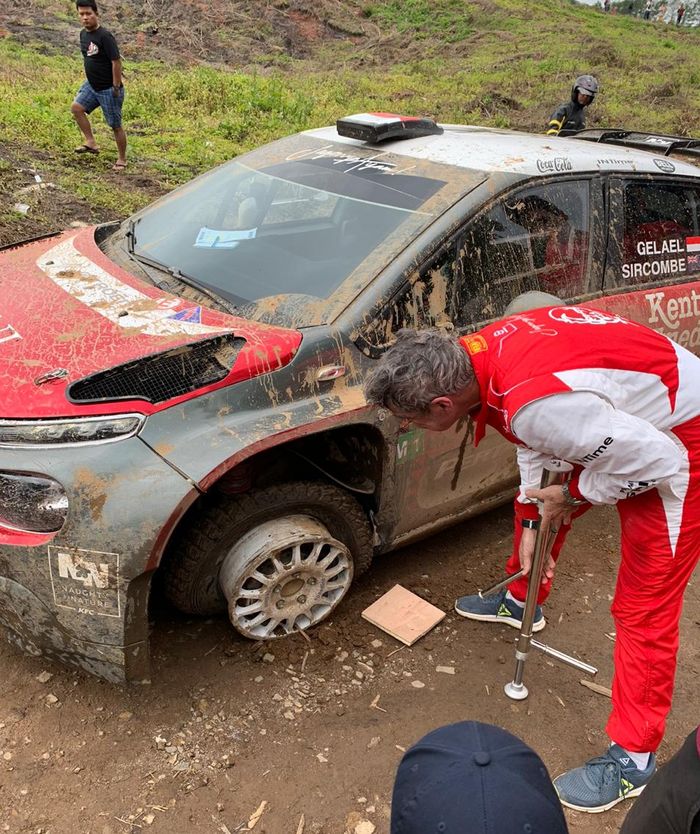 Co-driver Tiny Sircombe mengecek kerusakan roda depan kiri mobil Citroen C3 R5 yang dikemudikan Sean Gelael pada Danau Toba Rally 2019