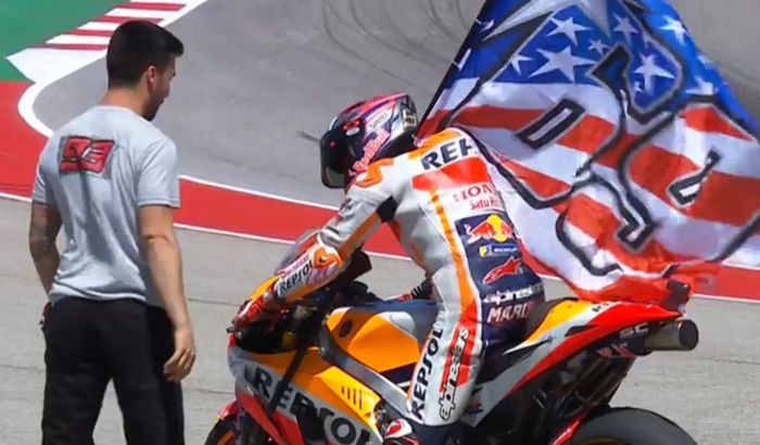 Marc Marquez merayakan kemenangan dengan mengibarkan bendera Nicky Hayden