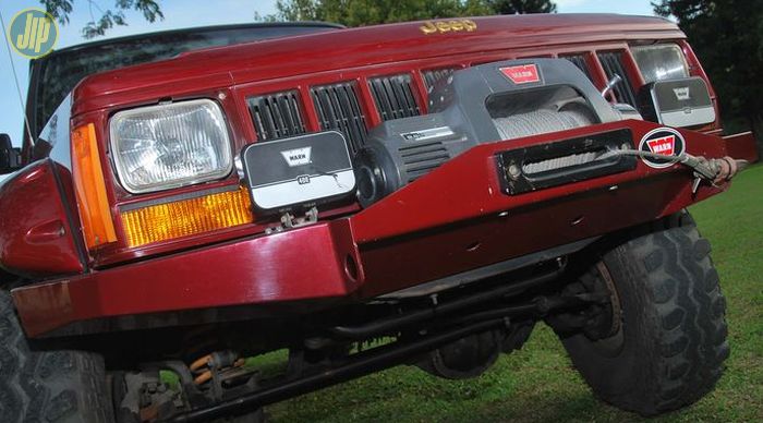 Jeep XJ Cherokee ini dipasangi bemper depan custom. Dipasangi lampu tembak tambahan dan winch Warn 9.5 Ti.