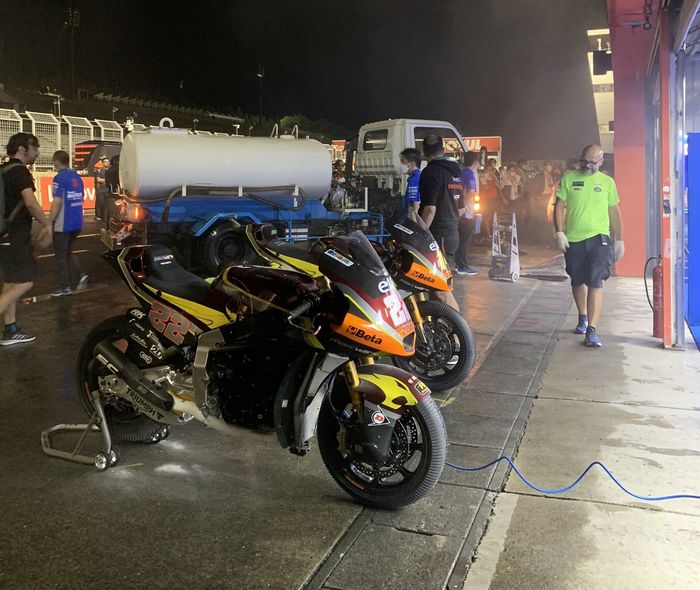 Mekanik Suzuki membantu dengan membersihkan motor tim Marc VDS selagi pemadam kebakaran memadamkan api