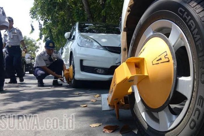 Petugas Dishub dan Polisi Lalu Lintas Polrestabes Surabaya menggembok mobil yang parkir sembarangan di bawah rambu larangan parkir di Jl Airlangga depan kampus B Unair, Rabu (13/9/2017).