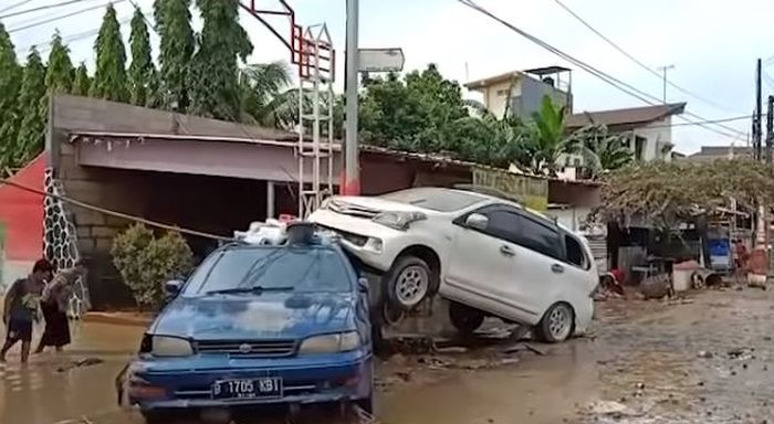 Toyota Avanza menindih sedan biru pasca banjir di kota Bekasi