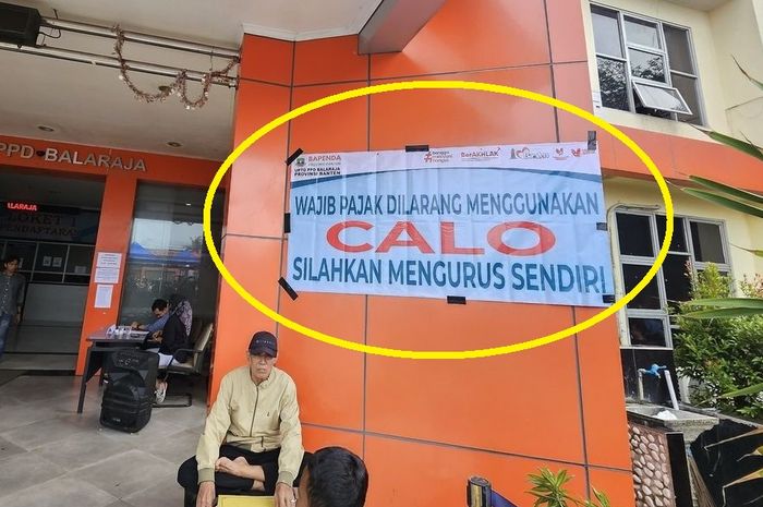 Dalam lingkaran kuning, tertempel spanduk bertuliskan 'WAJIB PAJAK DILARANG MENGGUNAKAN CALO, SILAHKAN MENGURUS SENDIRI' di Samsat Balaraja, Tangerang, Banten