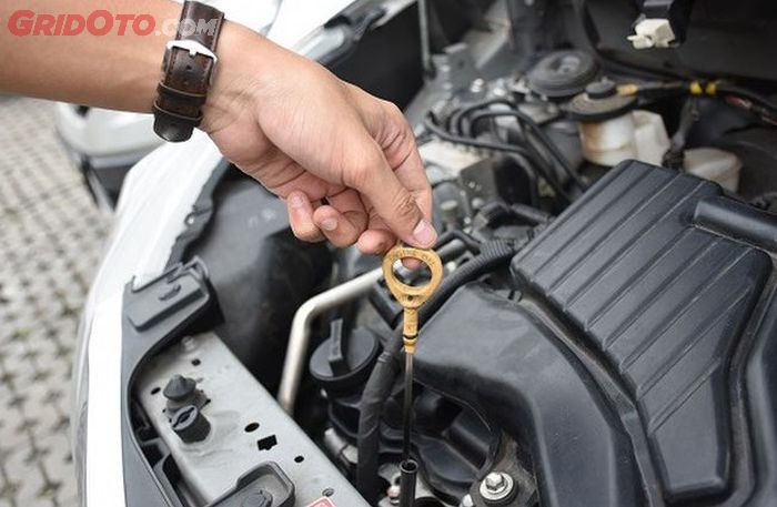Ilustrasi memeriksa kondisi oli mesin mobil melalui dipstick.
