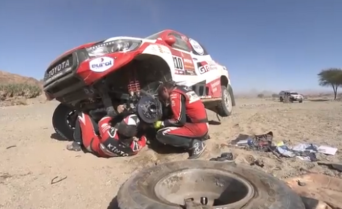 Fernando ALonso tiduran di bawah kolong mobil Toyota Hilux saat memperbaiki suspensi yang rusak di Dakar 2020