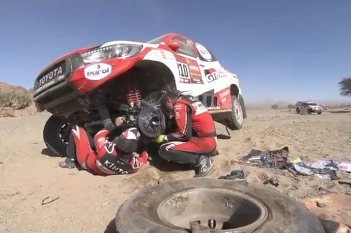 Fernando ALonso tiduran di bawah kolong mobil Toyota Hilux saat memperbaiki suspensi yang rusak di Dakar 2020