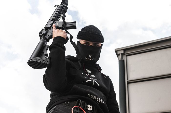 Ilustrasi orang dengan penutup muka membawa senjata api.