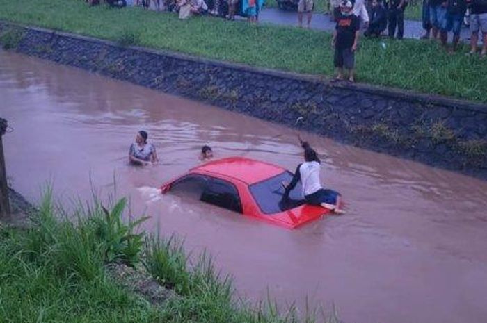 Sedan merah basah kuyup di saluran irigasi. Efek melaju kencang dan kaget hindari emak-emak bermotor