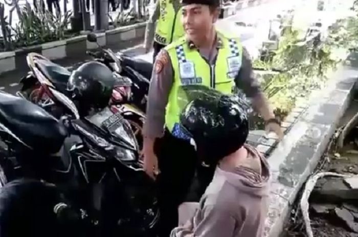 Cowok berbaju coklat dan pakai helm hitam duduk setelah ditenangkan polisi