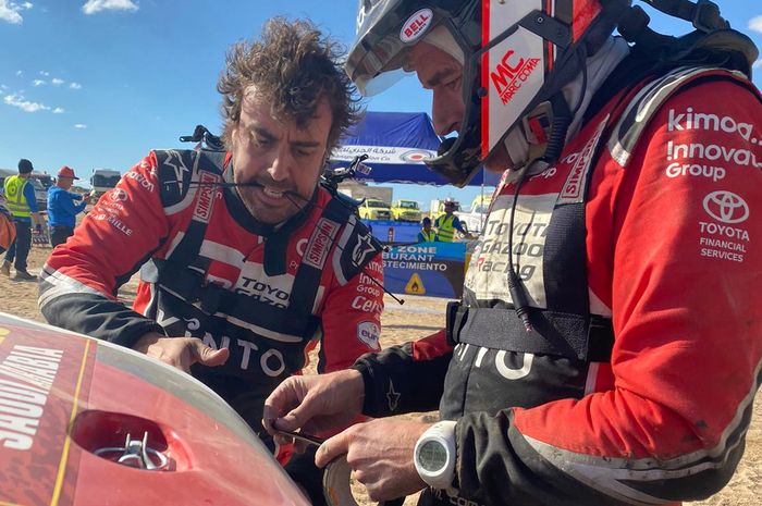Fernando Alonso mengigit cable tie saat memperbaiki bodi mobilnya di Reli Dakar 2020, dibantu Marc Coma