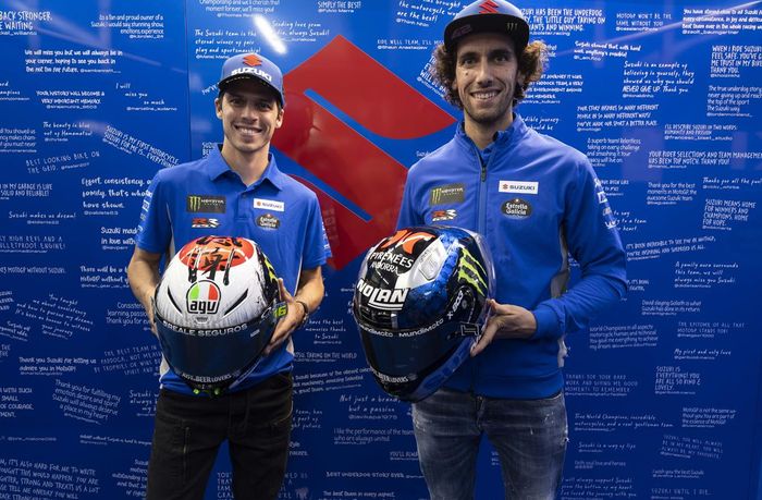 Joan Mir dan Alex Rins pada balapan terakhir mereka bersama tim Suzuki Ecstar di MotoGP Valencia 2022 dengan latar belakang ucapan dari para penggemar